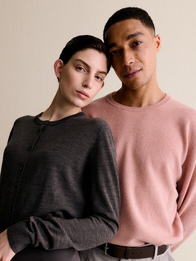 A woman in a grey sweater and a man in a pink sweater lean against each other in front of a light background and appear relaxed. | © Gabor Shoes GmbH, Germany