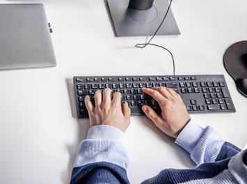 Person tippt auf externer Tastatur an Schreibtisch mit Laptop und Monitorfuß. | © Gabor Shoes GmbH, Rosenheim