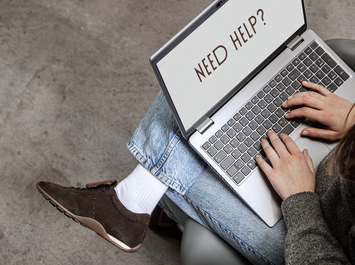 Person mit braunen Sneakern arbeitet am Laptop, auf dem „NEED HELP?“ zu lesen ist. | © Gabor Shoes GmbH, Rosenheim