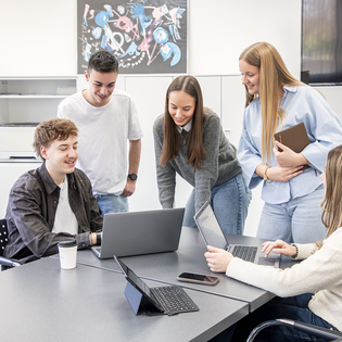 Fünf Personen stehen und sitzen um einen Besprechungstisch und arbeiten an Laptops. | © Gabor Shoes GmbH, Rosenheim