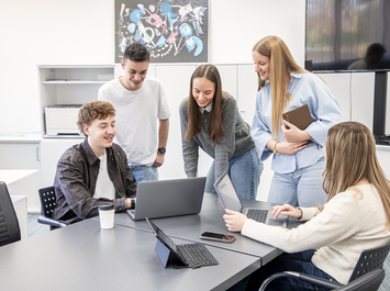 Fünf Personen stehen und sitzen um einen Besprechungstisch und arbeiten an Laptops. | © Gabor Shoes GmbH, Rosenheim