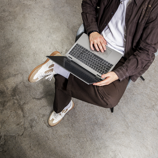 Person sitzt überkreuzt auf Stuhl und arbeitet mit aufgeklapptem Laptop. | © Gabor Shoes GmbH, Rosenheim