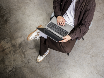 Person sitzt überkreuzt auf Stuhl und arbeitet mit aufgeklapptem Laptop. | © Gabor Shoes GmbH, Rosenheim