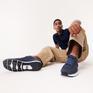 En man sitter avslappnat på golvet, har på sig beigea byxor, en blå topp och mörkblå sneakers. Skorna syns tydligt i förgrunden av bilden. | © Gabor Shoes GmbH, Tyskland