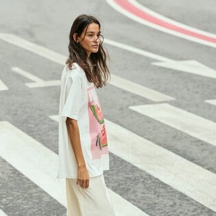 En kvinna går över ett övergångsställe och har på sig en vit t-shirt med färgglatt tryck samt ljusa byxor. Gatan har tydliga markeringar. | © Gabor Shoes GmbH, Tyskland