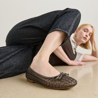 En kvinna ligger avslappnat på golvet och har på sig flätade mörkbruna ballerinaskor samt mörka jeans. | © Gabor Shoes GmbH, Tyskland