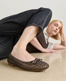 Eine Frau liegt entspannt auf dem Boden und trägt geflochtene Ballerinas in dunklem Braun sowie eine dunkle Jeans. | © Gabor Shoes GmbH, Rosenheim