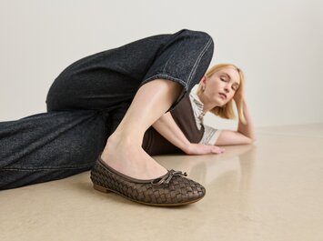 En kvinna ligger avslappnat på golvet och har på sig flätade mörkbruna ballerinaskor samt mörka jeans. | © Gabor Shoes GmbH, Tyskland