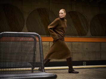 En kvinna går genom en tunnelbanestation och bär en brun stickad klänning med bruna knähöga stövlar från Gabor. | © Gabor Shoes GmbH, Tyskland