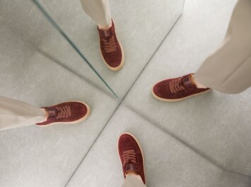 Eine Frau mit beigefarbener Hose trägt bordeauxrote Sneaker und steht vor zwei Spiegeln, sodass die Schuhe mehrfach reflektiert werden. | © Gabor Shoes GmbH, Rosenheim