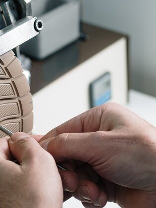 Nahaufnahme von Händen, die eine helle Schuhsohle an einer Metallvorrichtung bearbeiten. | © Gabor Shoes GmbH, Rosenheim