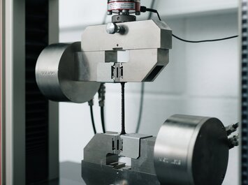 Una macchina di prova in metallo trattiene una stretta striscia di prova tra due dispositivi di presa per un test di trazione. | © Gabor Shoes GmbH, Germania