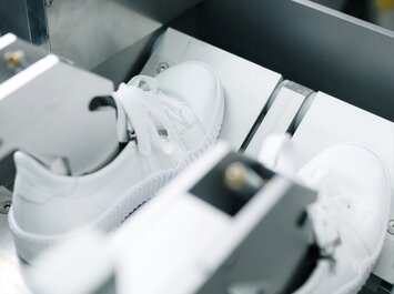 Due scarpe da ginnastica bianche sono fissate una accanto all’altra in una macchina di prova. | © Gabor Shoes GmbH, Germania