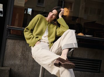 Una donna è seduta a terra e indossa un completo giallo con cintura e sandali beige con tacco ed effetto pelle di serpente. Lo sfondo è semplice e luminoso. | © Gabor Shoes GmbH, Germania