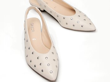Nahaufnahme eines Paars cremefarbener Gabor Slingpumps mit spitzer Kappe, dekoriert mit silbernen Nieten, auf weißem Hintergrund. | © Gabor Shoes GmbH, Rosenheim
