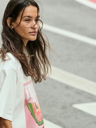 En kvinna går över ett övergångsställe och har på sig en vit t-shirt med färgglatt tryck. Gatan har tydliga markeringar. | © Gabor Shoes GmbH, Tyskland