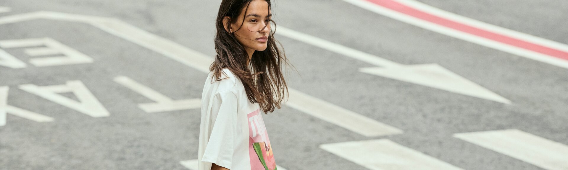 En kvinna går över ett övergångsställe och har på sig en vit t-shirt med färgglatt tryck. Gatan har tydliga markeringar. | © Gabor Shoes GmbH, Tyskland