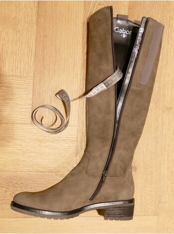 Ein brauner Stiefel von Gabor mit geöffnetem Reißverschluss liegt auf einem Holzboden. Ein Maßband ist um den Schaft des Stiefels gelegt. | © Gabor Shoes GmbH, Rosenheim