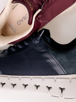 Eine Frau sitzt auf dem Boden und trägt rosa Sneakers mit weißen und rosafarbenen Socken. Die Hand berührt die Schuhsohle, der Hintergrund ist weiß und schlicht. | © Gabor Shoes GmbH, Rosenheim
