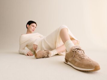 Une femme est allongée de façon détendue sur le sol devant un fond clair, porte une robe en maille crème et des baskets beiges de Gabor avec une semelle claire. | © Gabor Shoes GmbH, Allemagne