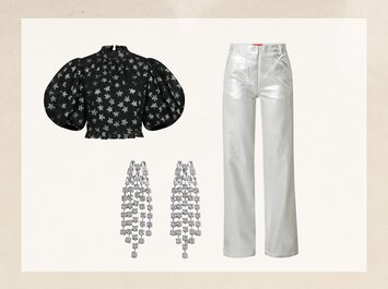 Svart blus med silverfärgat stjärnmönster och ballongärmar, silverfärgade raka byxor och ett par långa silverörhängen med många små stenar. Kläderna och accessoarerna är arrangerade mot en ljus bakgrund. | © aboutyou.de 