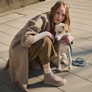 Schwarze, strukturierte Stiefeletten mit grober Sohle stehen auf einer Metallplatte im trockenen, hohen Gras. Die Frau trägt eine dunkelrote Hose. | © Gabor Shoes GmbH, Rosenheim