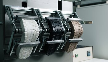 Drei verschiedenfarbige Schuhsohlen sind in einer Prüfmaschine eingespannt. | © Gabor Shoes GmbH, Rosenheim