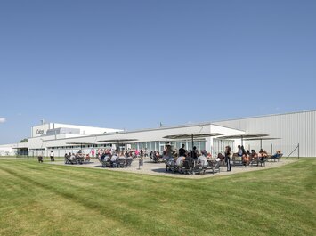 Menschen sitzen und stehen auf einer Terrasse vor einem Gabor-Firmengebäude. | © Gabor Shoes GmbH, Rosenheim