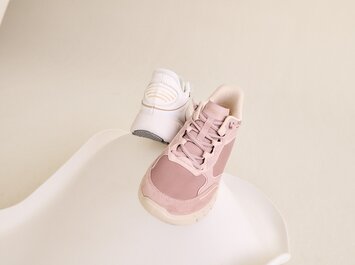 Gabor Damenschuhe | Zwei FlexFlex Damen-Sneaker in Rosa und Weiß auf heller, geschwungener Fläche vor neutralem Hintergrund. Der weiße Sneaker ist von hinten fotografiert, der rosane frontal. | © Gabor Shoes GmbH, Rosenheim